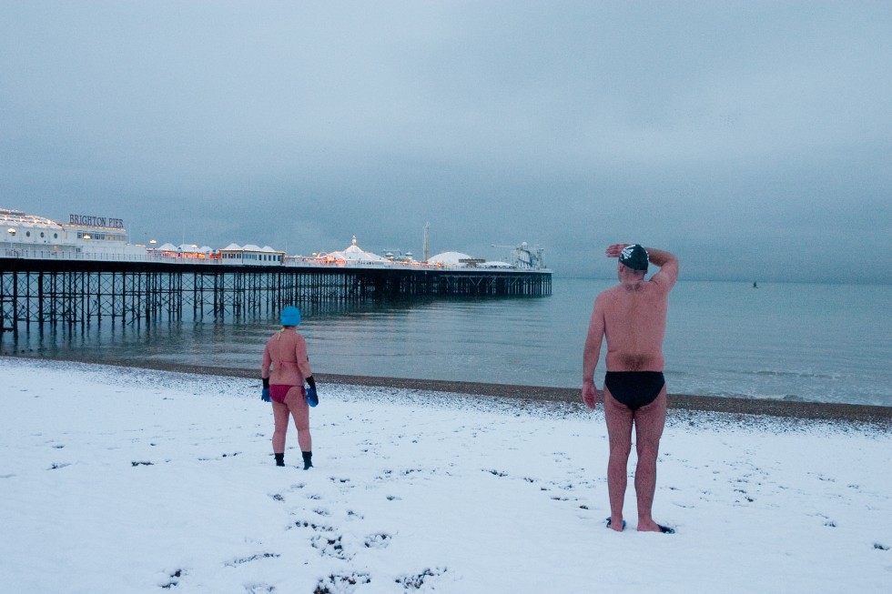 Two swimmers look out to sea on a snow covered beach